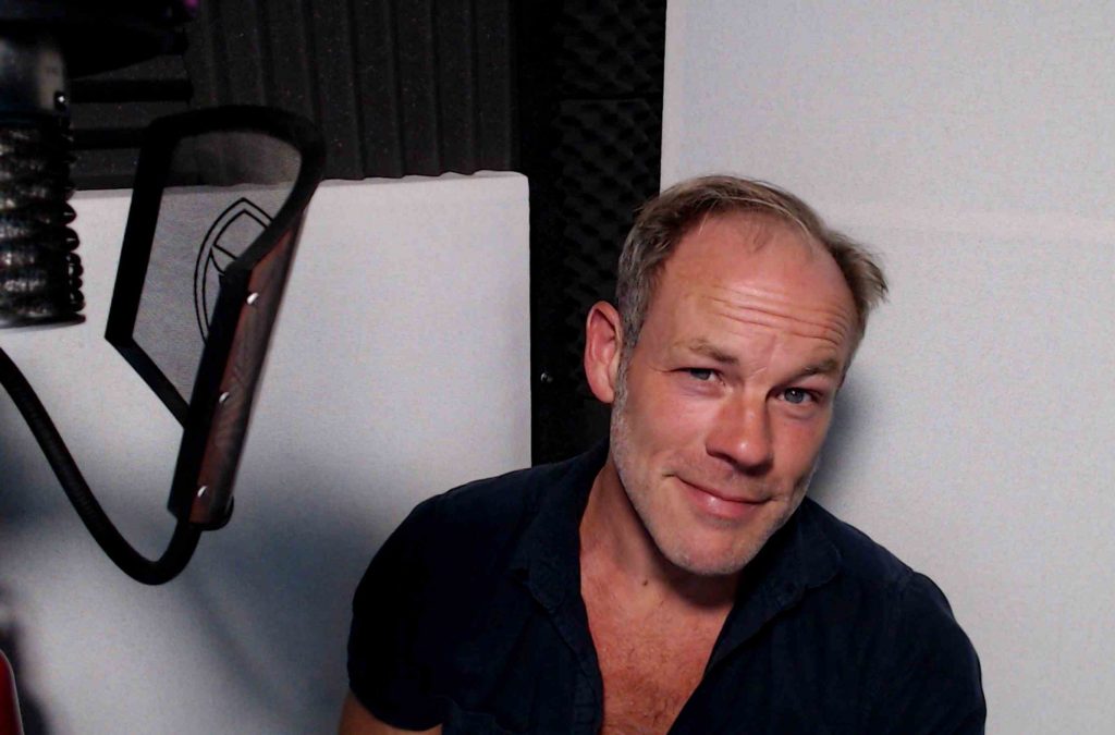 English voice actor Anthony Hewson in his recording booth - head and shoulders photograph with microphone and pop filter just in shot